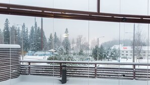 Une vue extérieure enneigée depuis un balcon doté d’une rambarde en métal, avec des arbres et un bâtiment sur lequel est affiché un panneau indiquant une « vente ».