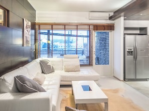 Una sala moderna con un sofá blanco, una mesa de centro y una cocina con refrigerador.