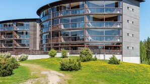 Un bâtiment moderne à plusieurs étages, doté d’une façade incurvée, de grandes fenêtres en verre et d’une combinaison de matériaux en bois et en métal.