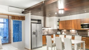 Une cuisine moderne dotée d’un réfrigérateur encastré, de meubles en bois et d’un coin repas avec des chaises blanches.