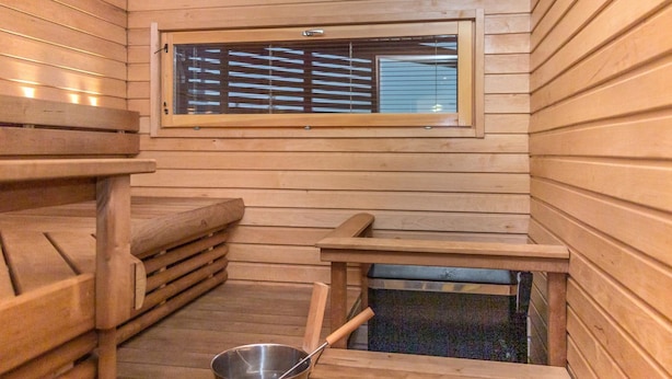 Un sauna avec des murs en bois, une fenêtre, un banc et un seau.