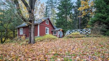 Une cabane rouge avec un petit porche, entourée d’arbres et d’une clôture en bois.