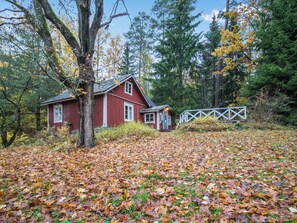 A red cabin with a small porch, surrounded by trees and a wooden fence.