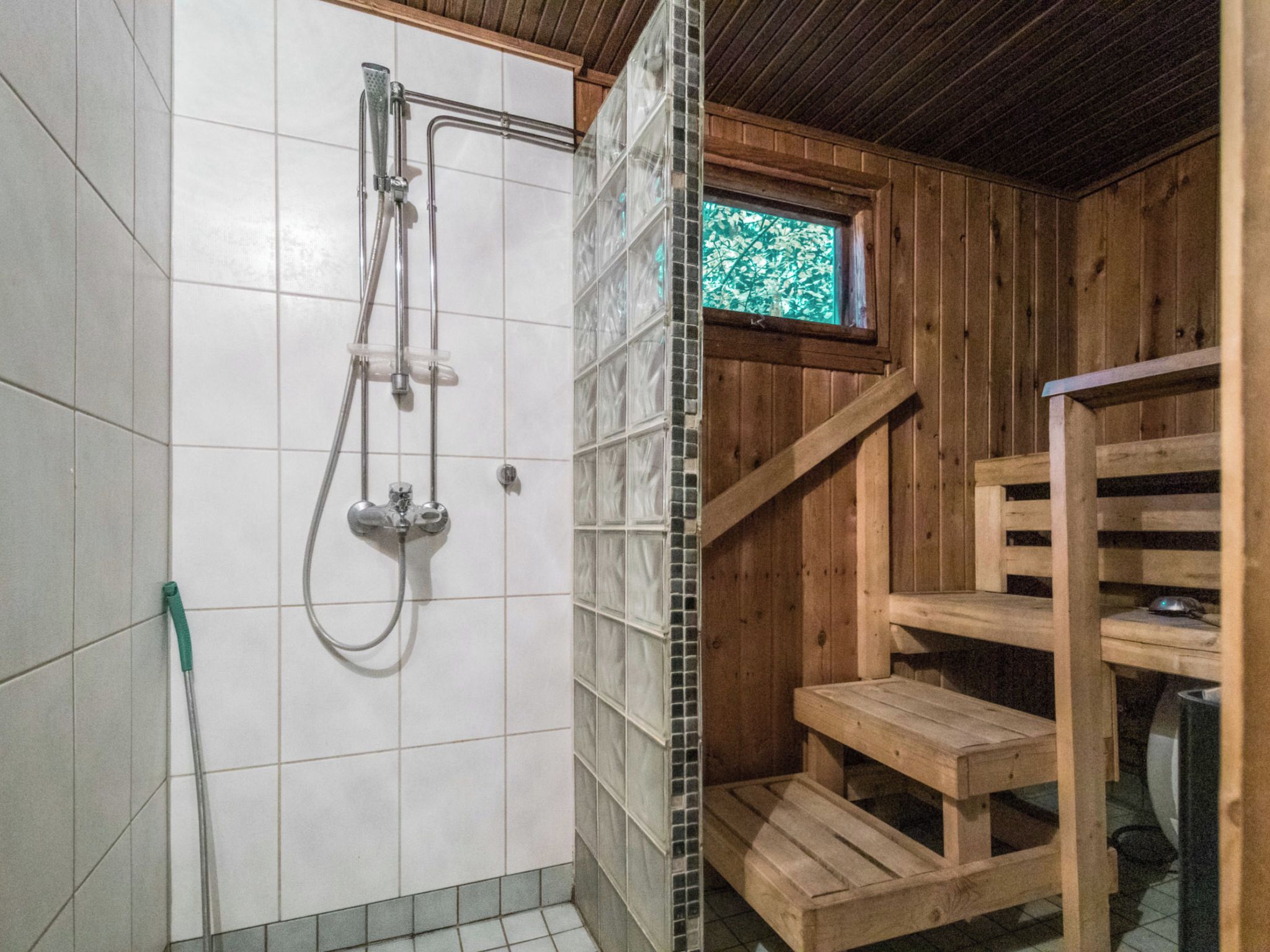 A wooden cabin with a shower area, a window, and a wooden staircase.