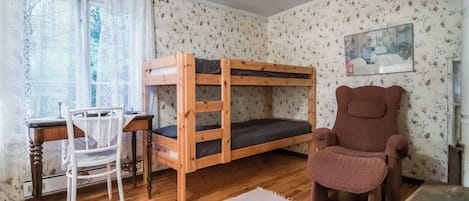 A bunk bed room with a desk and chair, a wooden table, and a patterned wall.
