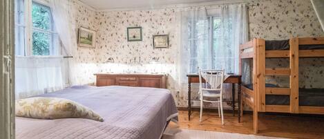Een slaapkamer met een bed, een bureau, een stoel, een kledingkast en een raam met gordijnen.