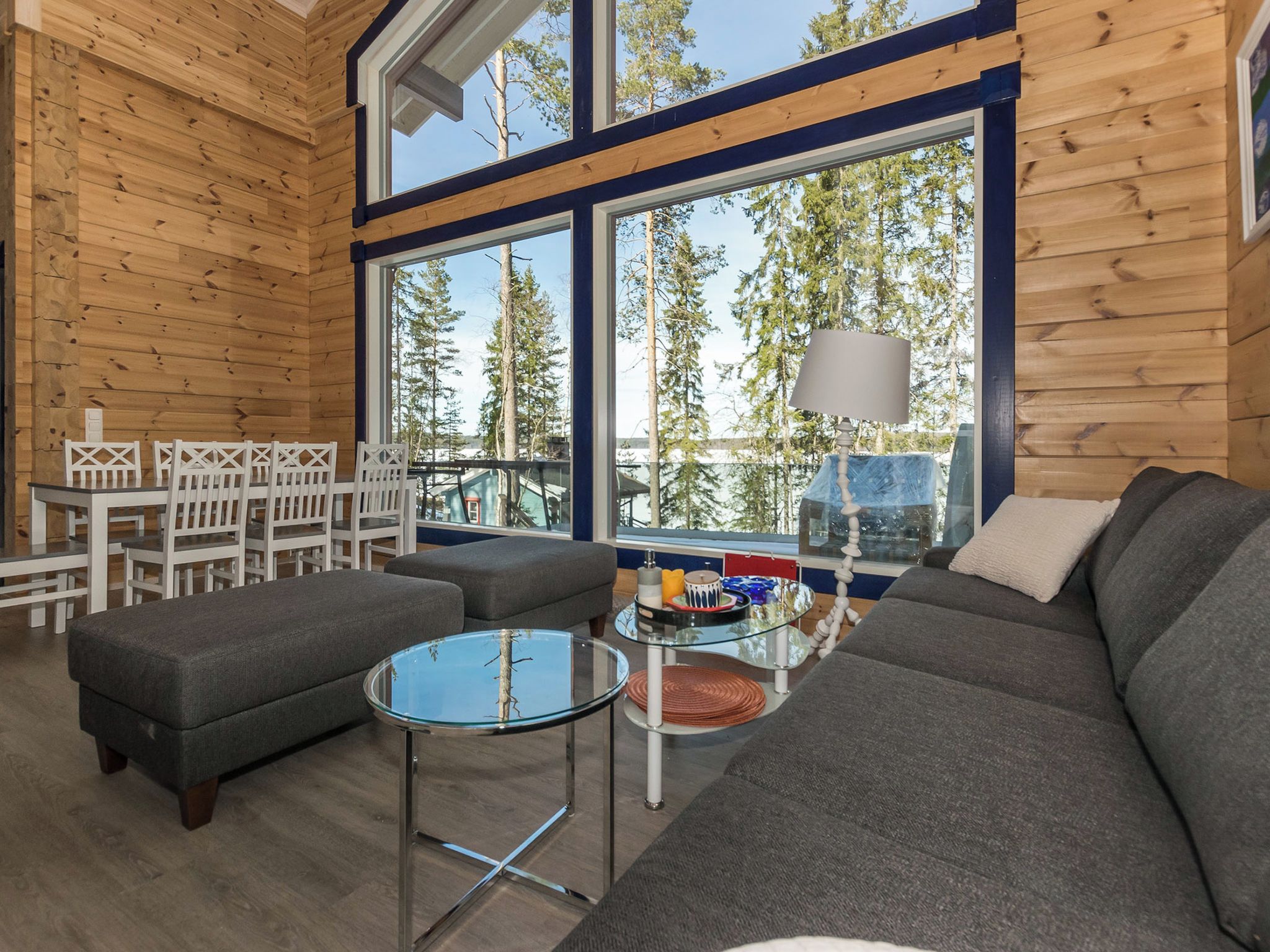 Ein modernes Interieur einer Blockhütte mit einem großen Fenster, einer Couch, einem Glastisch und einem Essbereich.