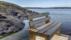 A wooden bench on a dock by a calm lake with rocky shores and a clear sky.