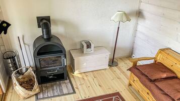Una habitación acogedora con una estufa de leña, un caja de almacenamiento blanco, una lámpara, una cesta tejida y un banco de madera.