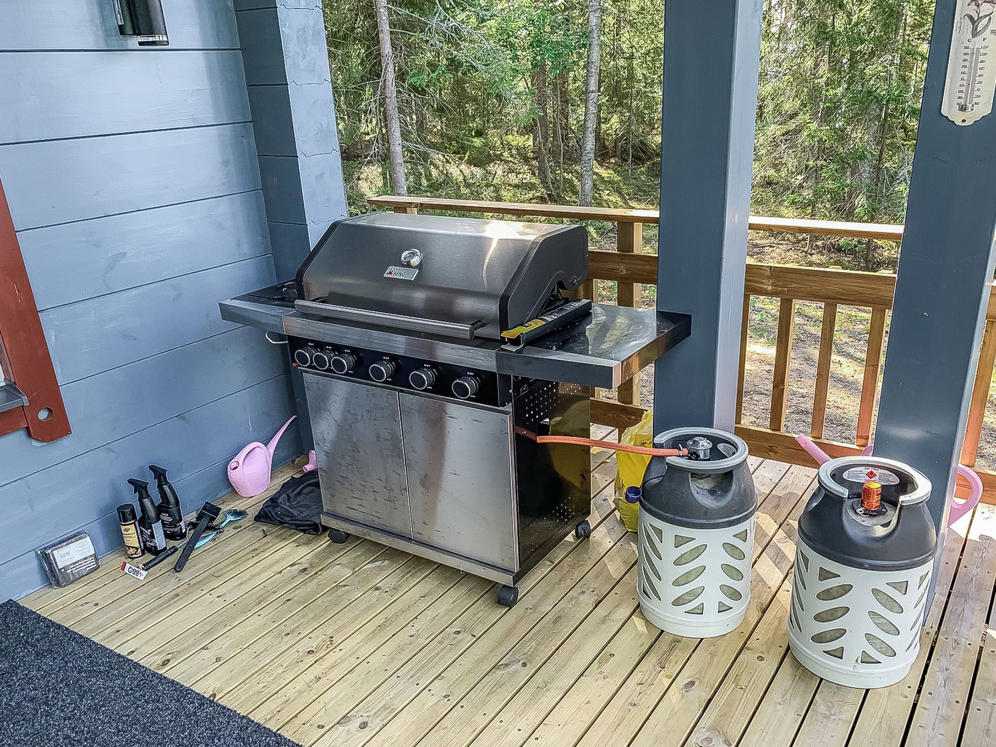 A barbecue grill on a wooden deck with a blue wall and a wooden railing in the background.