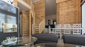 A modern interior with a glass table, grey sofas, wooden walls, and a staircase.