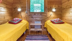 A cabin with two beds, each with a yellow blanket and a red pillow, a small table, and a window with a view of trees.