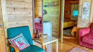 A cozy wooden cabin interior with a teal armchair, a small white table, and a red rug.