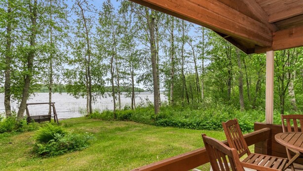 A wooden deck with a table and chairs overlooking a lake surrounded by trees.