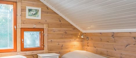Mökki, jossa on kaksi sänkyä, pieni lipasto, ikkuna, jossa on sälekaihtimet, ja uloskäynnin opastekyltti.