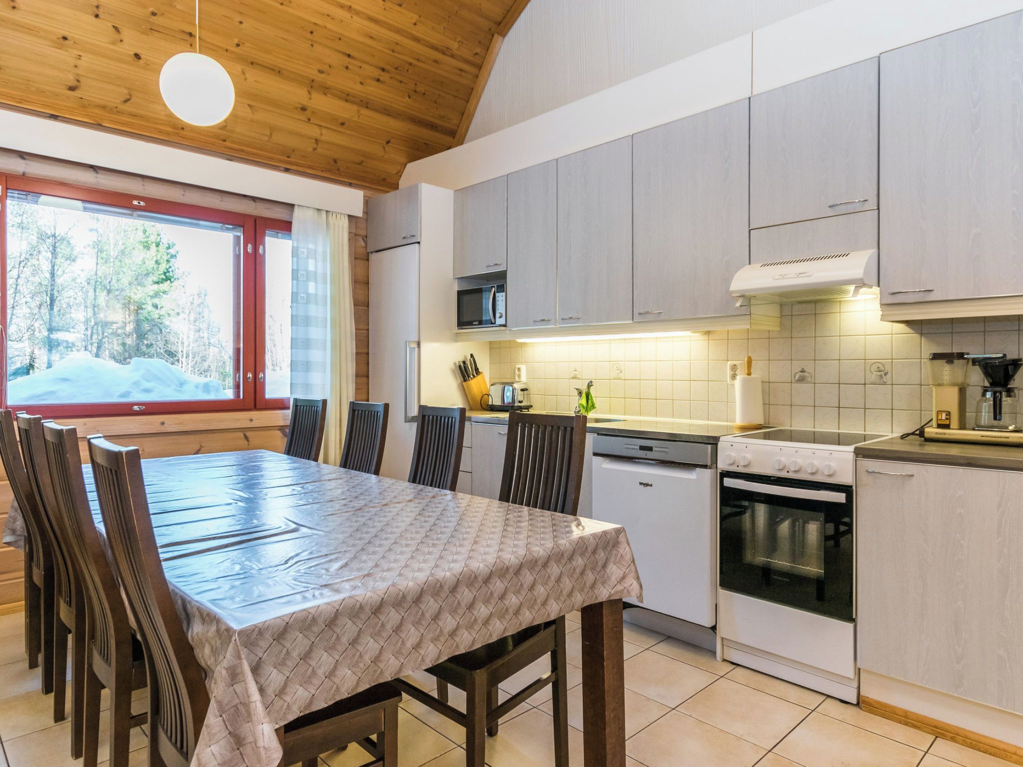 Moderni keittiö, jossa on puiset kaapit, ruokapöytä tuoleineen ja ikkunasta avautuva näkymä lumiseen maisemaan.