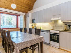 A modern kitchen with wooden cabinets, a dining table with chairs, and a view of a snowy landscape through a window.