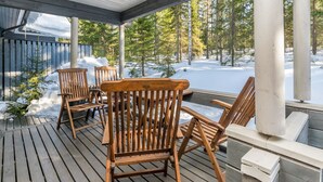 Eine Holzterrasse mit Stühlen und einem Tisch, mit Blick auf eine verschneite Landschaft mit Bäumen.