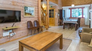 Ein Holzblockhaus-Interieur mit Fernseher, Sitzgelegenheiten, einem Essbereich und einer Treppe.
