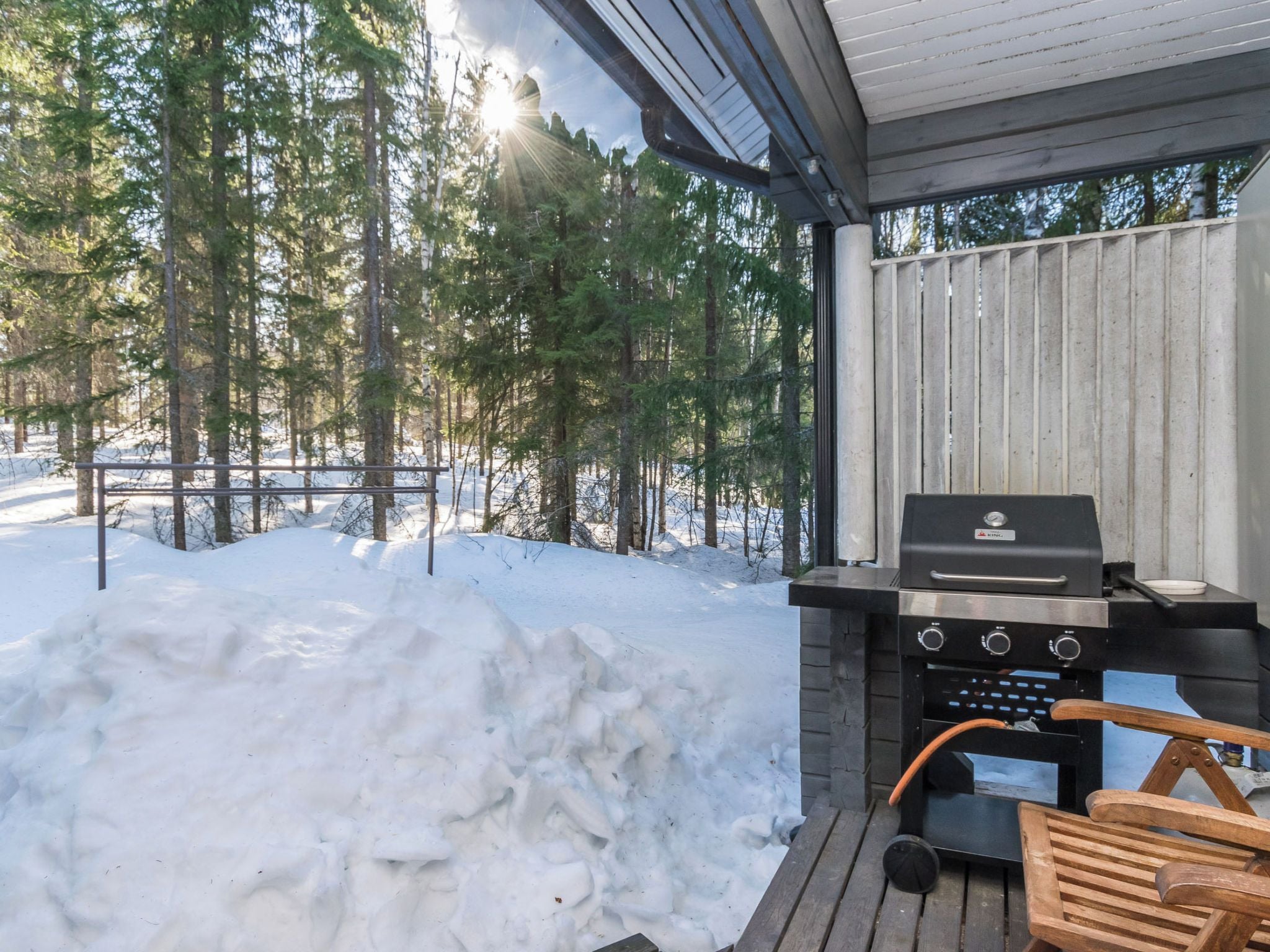 Un espacio al aire libre techado con una parrilla, una silla de madera y suelo cubierto de nieve.