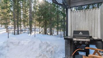 Un espacio al aire libre techado con una parrilla, una silla de madera y suelo cubierto de nieve.