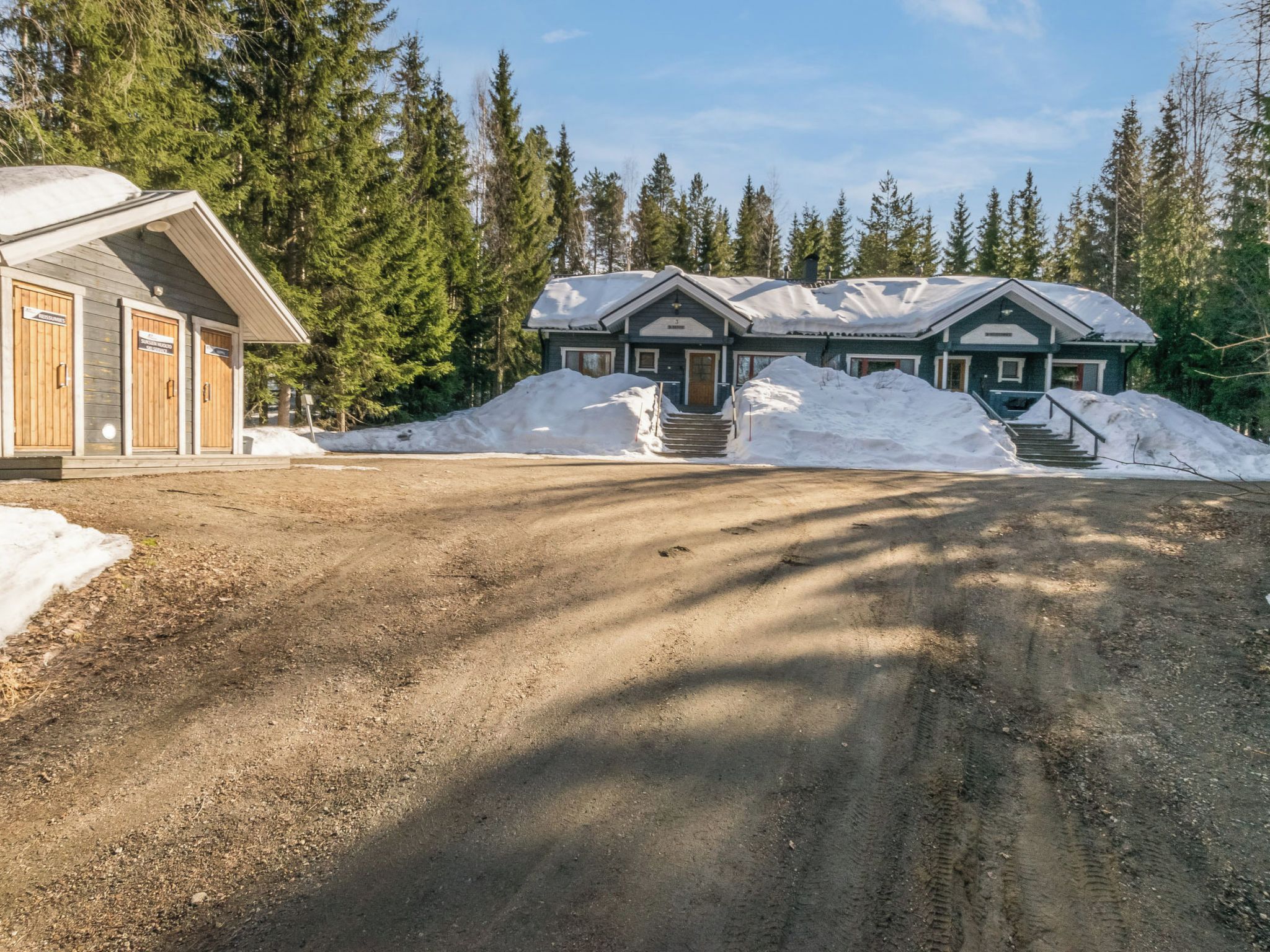 Kaksikerroksinen mökki, jonka eteen johtaa soratie, ja mökin edessä on portaikko.