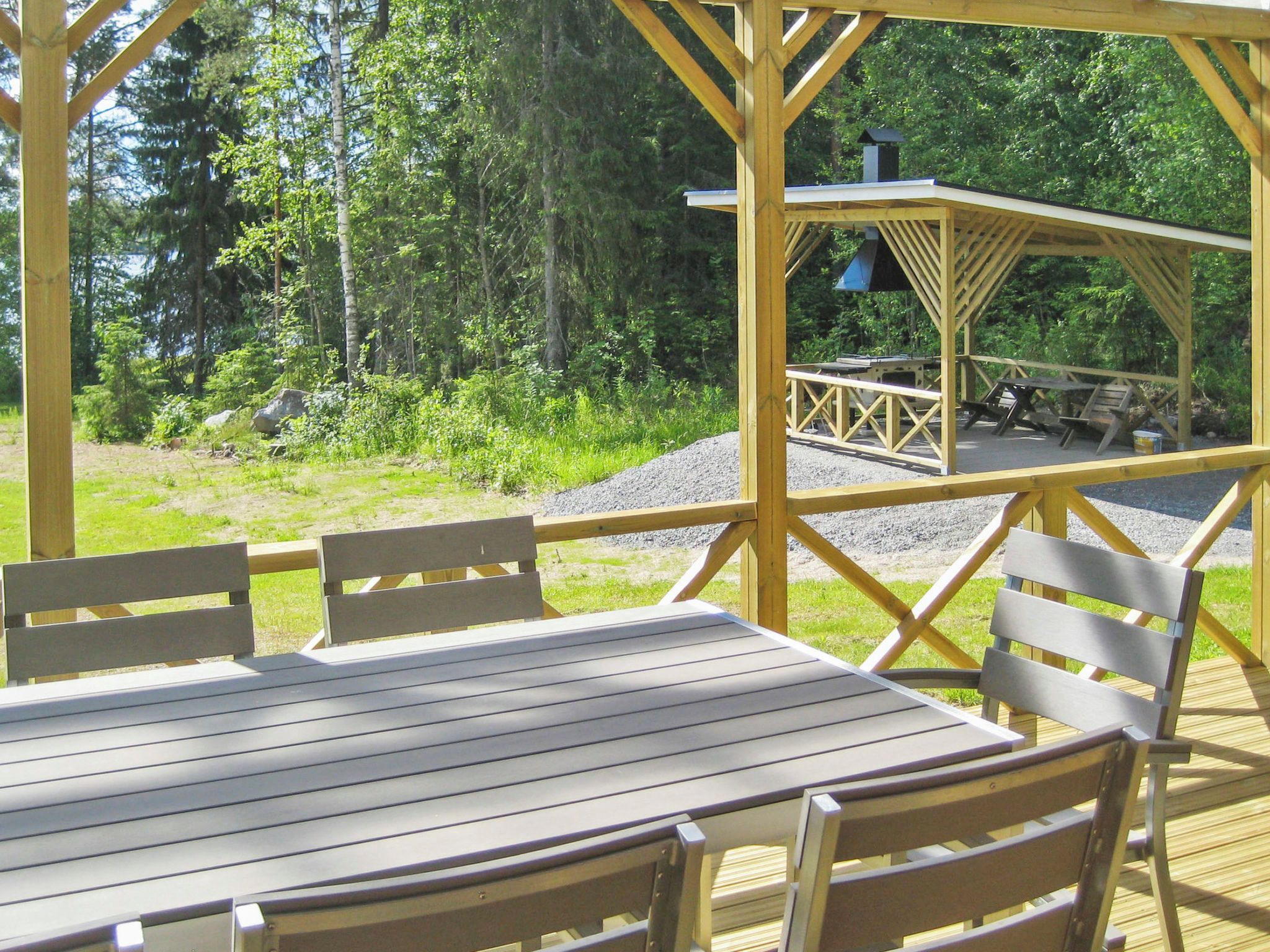 A wooden deck with a table and chairs, overlooking a forested area with a picnic table and grill.