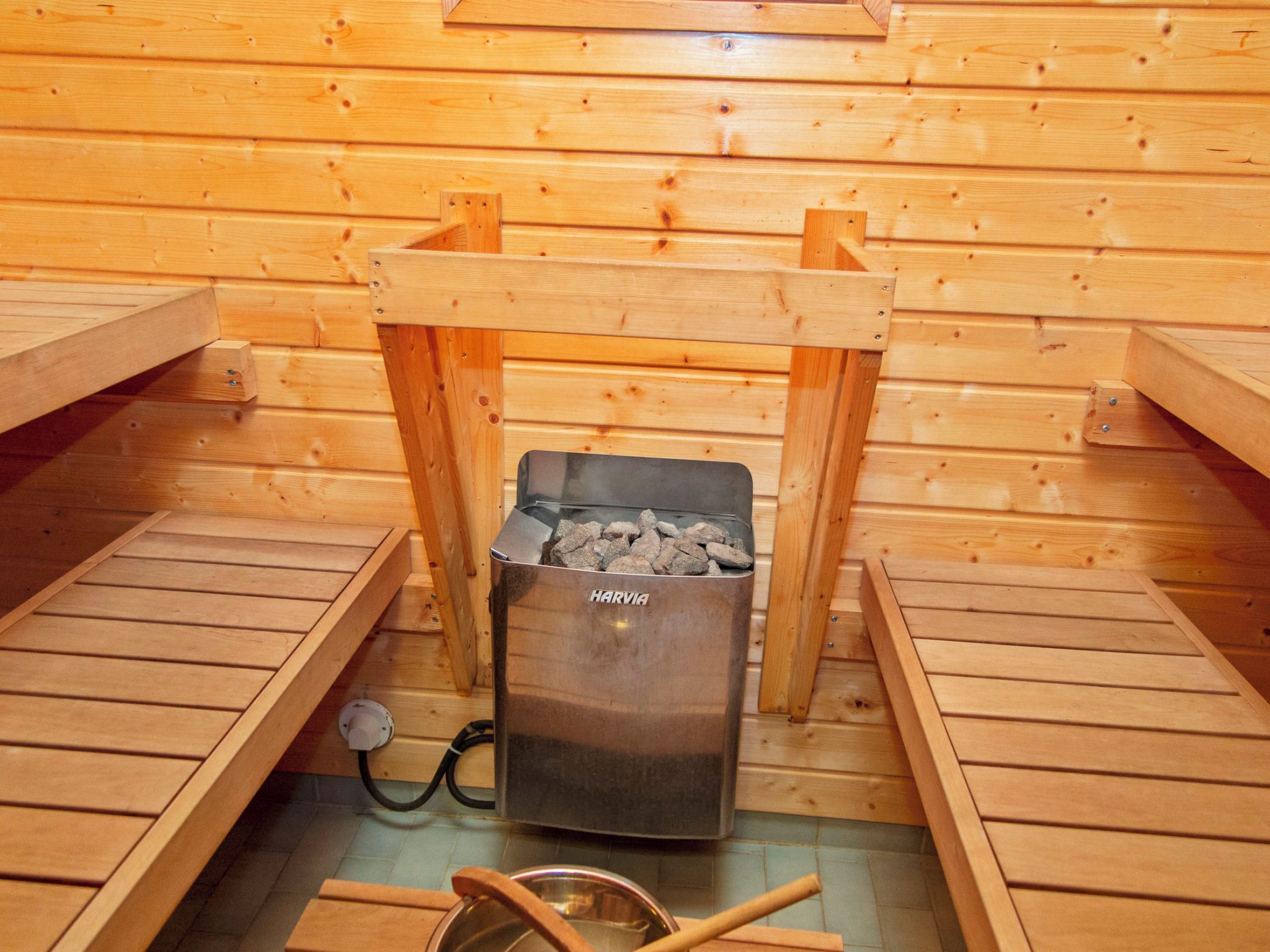 Un sauna comprenant un espace avec un récipient en métal portant l’inscription « HARVIA » pour les pierres, des bancs en bois et un seau en métal.