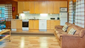 A cozy cabin-style room with wooden floors, a sofa, a kitchen with wooden cabinets, a microwave, and a stove. - Rinnepelto by Interhome (Nilsiä)