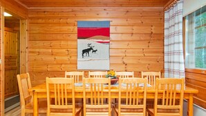 A wooden-paneled room with a dining table and chairs, a painting of deer on the wall, and a window with curtains. - Rinnepelto by Interhome (Nilsiä)