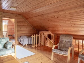 A cozy attic room with wooden walls and a sloped ceiling. It includes a bed, a chair, a sofa, and a small table.