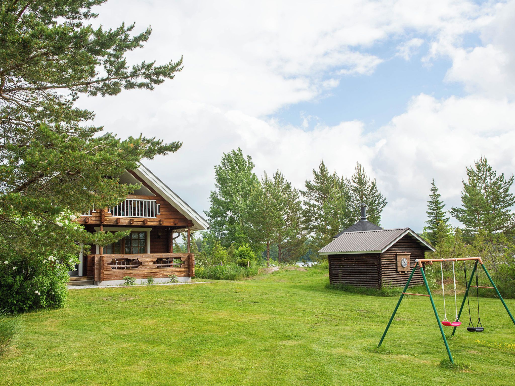 Eine Holzhütte mit einer Holzterrasse und einer Schaukel im grünen Garten.