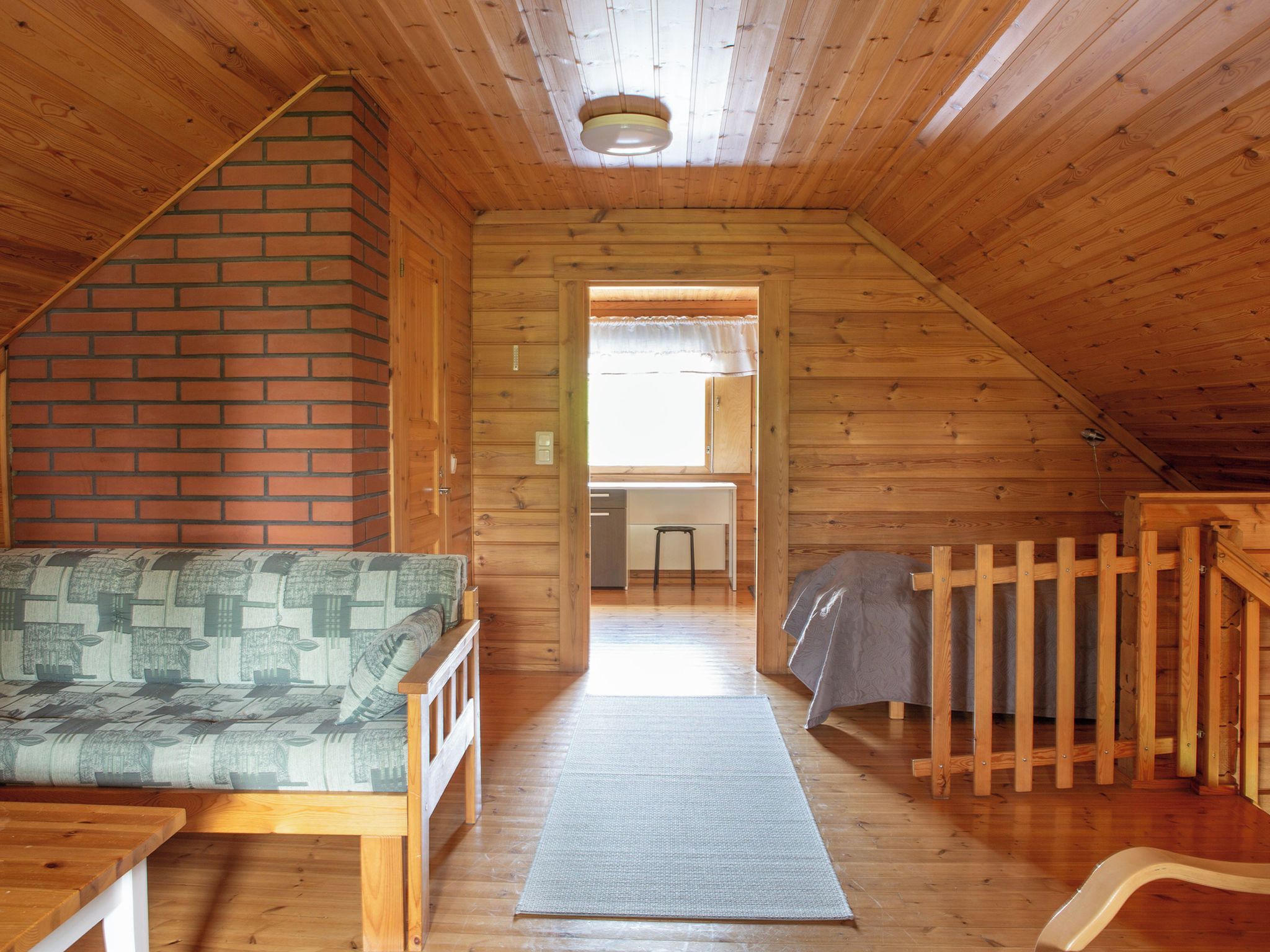 Un interior de madera con un sofá, una mesita, un banco y una cocina visible a través de una puerta abierta.