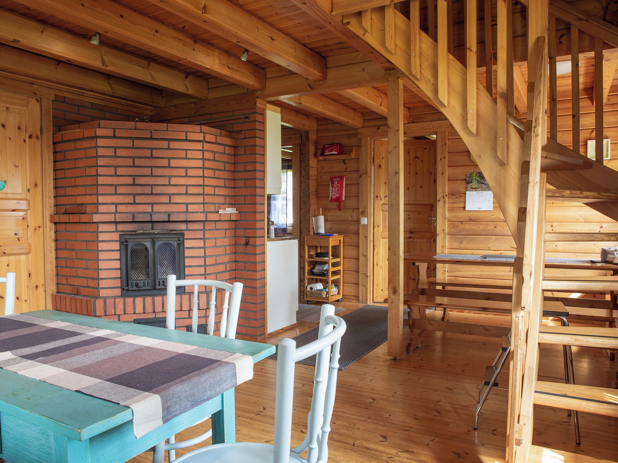 A wooden interior with a brick fireplace, a dining table with chairs, and a wooden staircase.