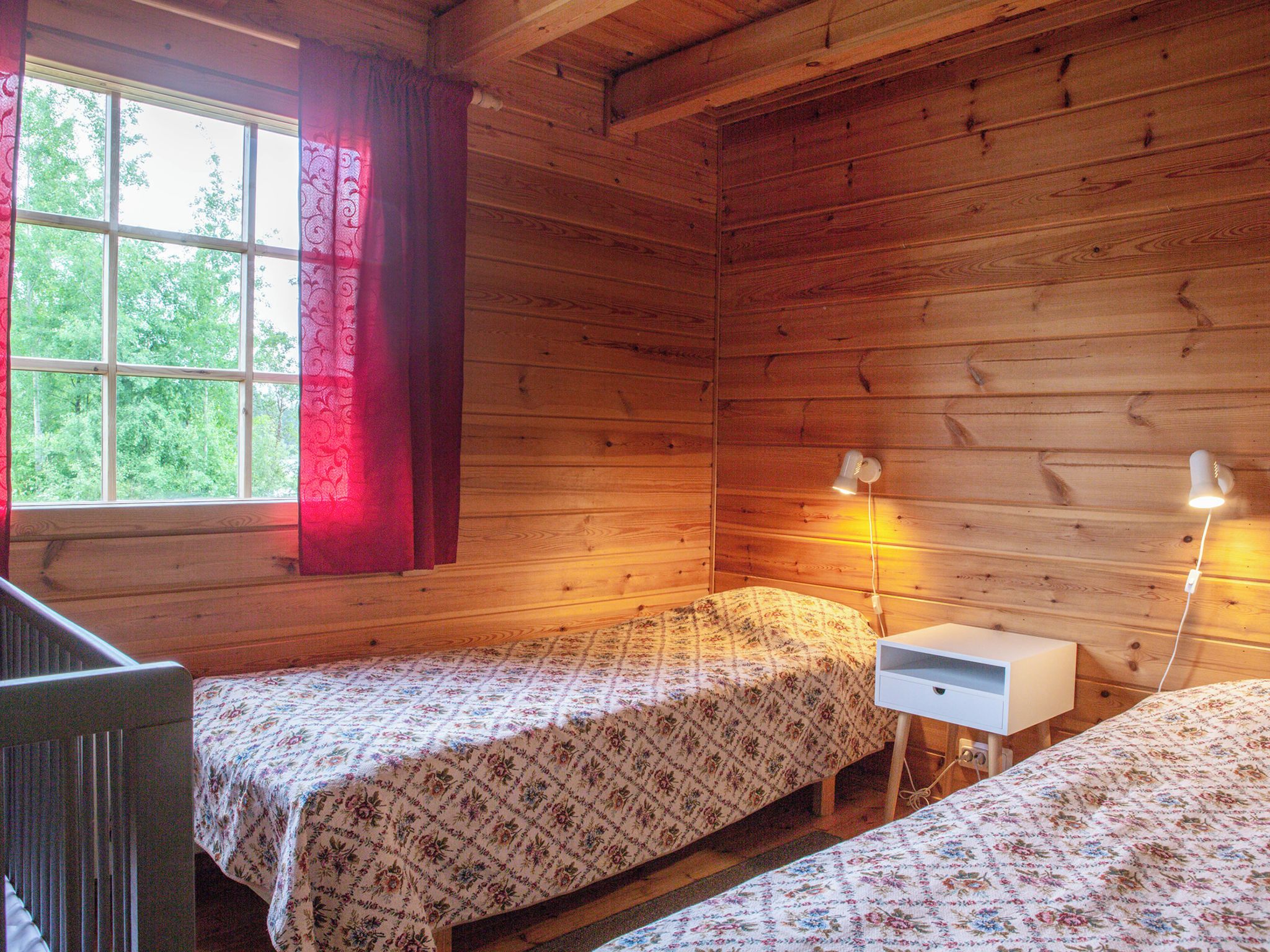 A cabin with two beds, a window with curtains, and a nightstand with a lamp.