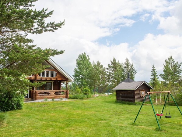A wooden cabin with a porch and a swing set in a grassy yard.
