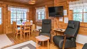A cozy cabin interior with wooden walls, a dining area with a table and chairs, a TV mounted on the wall, and a window with curtains. - Auringonlasku by Interhome (Punkaharju)
