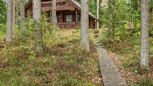 A cabin with a wooden exterior, surrounded by tall trees and a wooden pathway leading to it. - Auringonlasku by Interhome (Punkaharju)