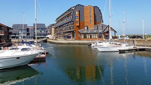 A marina with several boats docked, a modern building with a unique architectural design, and a clear blue sky. - Les Marinas by Interhome (Deauville-Trouville)