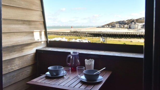 A balcony with a wooden table set for two, overlooking a beach and pier. - Les Marinas by Interhome (Deauville-Trouville)