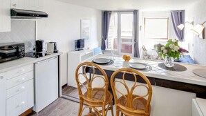 A modern kitchen with white cabinets, a black range hood, and a dining area with two wicker chairs and a table set for two. - Les Marinas by Interhome (Deauville-Trouville)