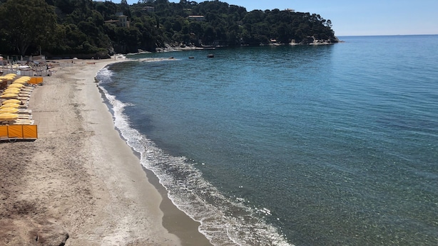 Une plage à l’eau d’un bleu limpide, avec un rivage sablonneux et une rangée de parasols jaunes.