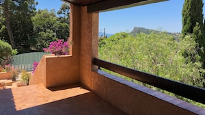 Un espace extérieur abrité offrant une vue sur un jardin luxuriant et des collines lointaines.
