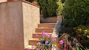 Un escalier menant à un bâtiment dont la façade est ornée d’un revêtement texturé, le tout étant entouré de différentes plantes et fleurs.