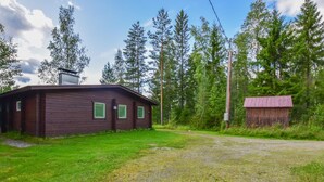 A rustic cabin with a metal roof, surrounded by a grassy area and dense forest. - Sieralahden lomakylä, mökki 1 by Interhome (Savonlinna)