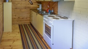 A compact kitchen with wooden walls, a stove, a sink, and a small cabinet. - Sieralahden lomakylä, mökki 1 by Interhome (Savonlinna)