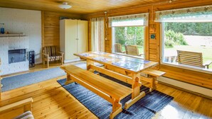 A wooden cabin with a dining table, benches, a fireplace, and large windows overlooking a forested area. - Sieralahden lomakylä, mökki 1 by Interhome (Savonlinna)
