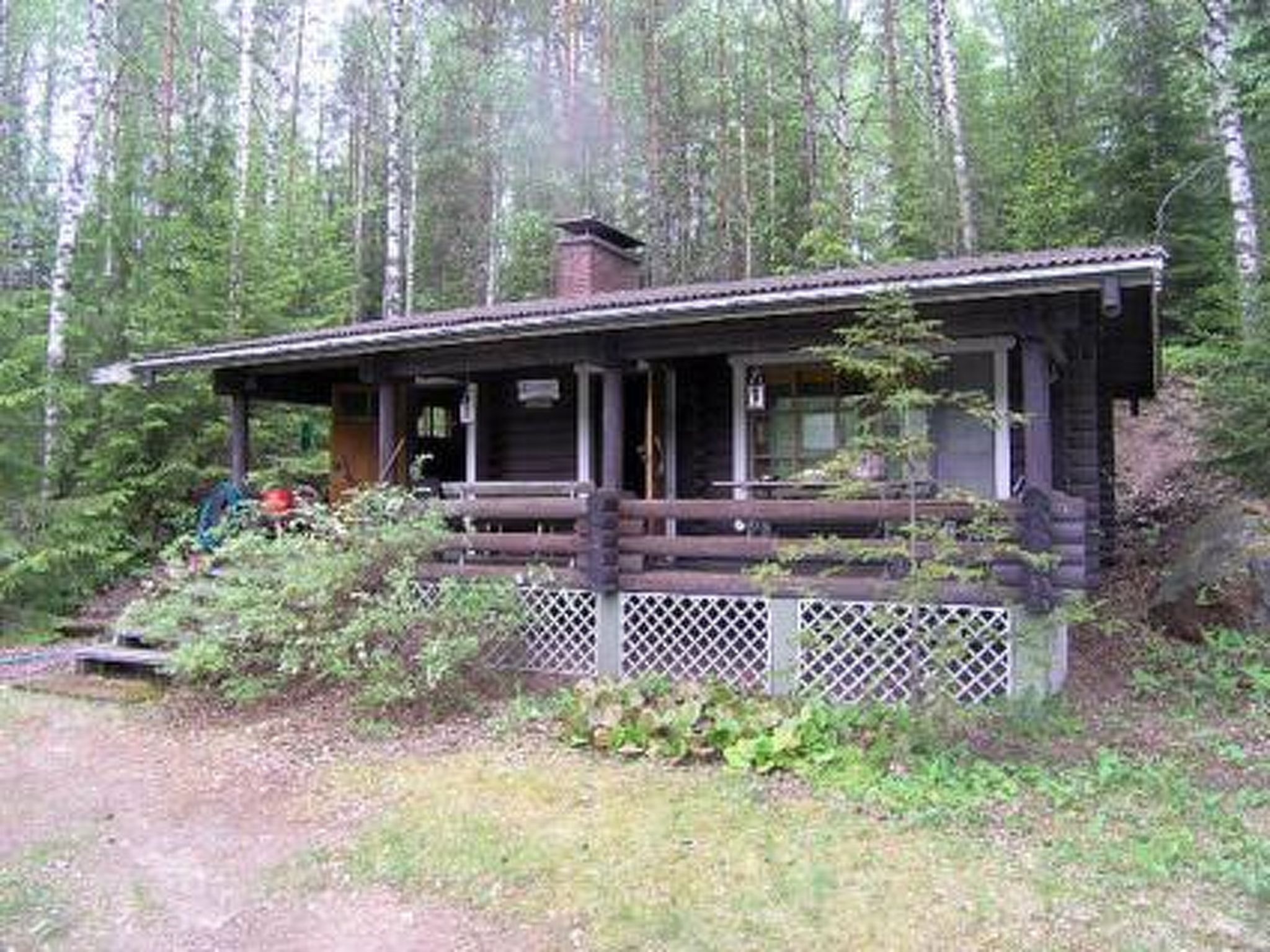 A rustic cabin with a porch, surrounded by dense forest.