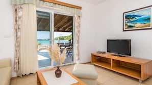 Un salón moderno con televisor, una mesa de centro de madera y vista al mar a través de un ventanal corredera.