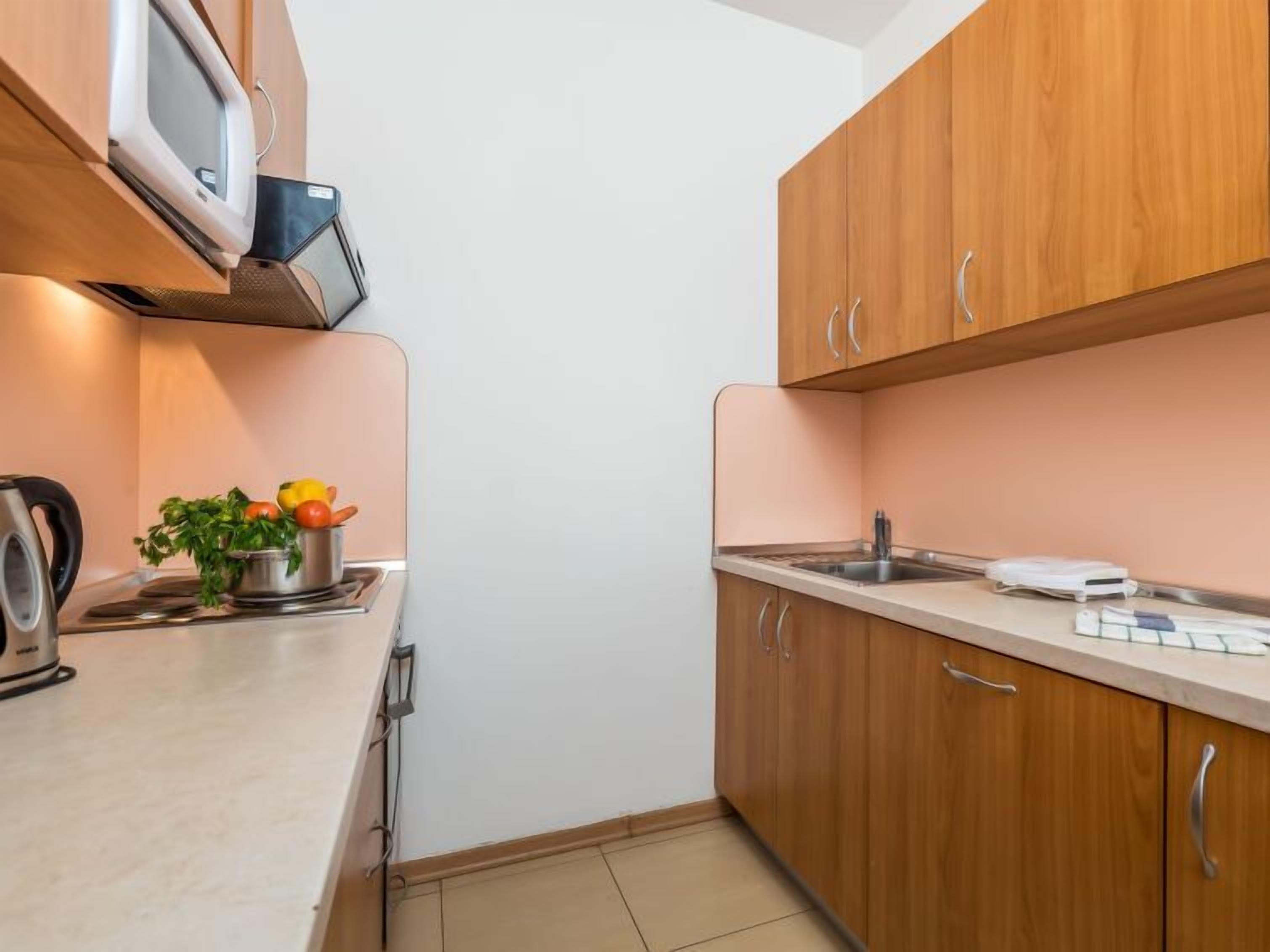 Una cucina compatta con mobili in legno, un forno a microonde, un bollitore e un piccolo vaso con una pianta sul piano di lavoro.